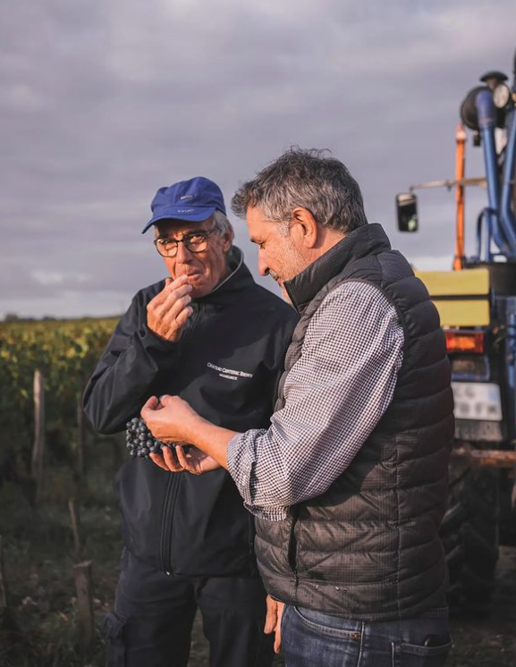 José Sanfins is tasting a grape in the vineyards with one member of his team.